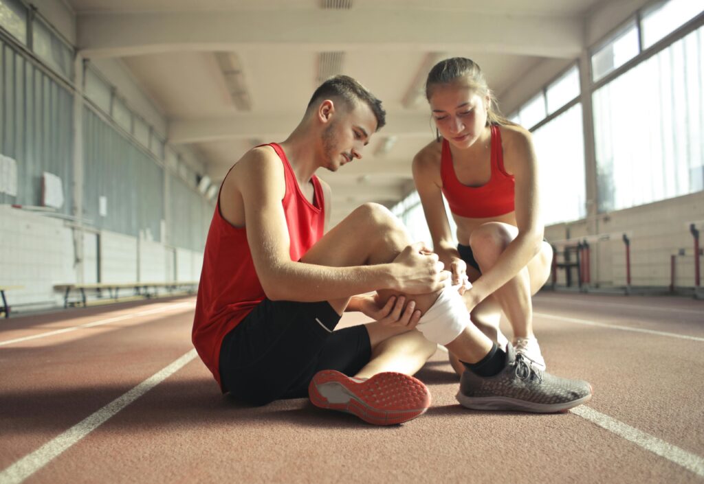 pexels-photo-3760275-3760275 A woman helps an injured man's leg on an indoor track, providing first aid.